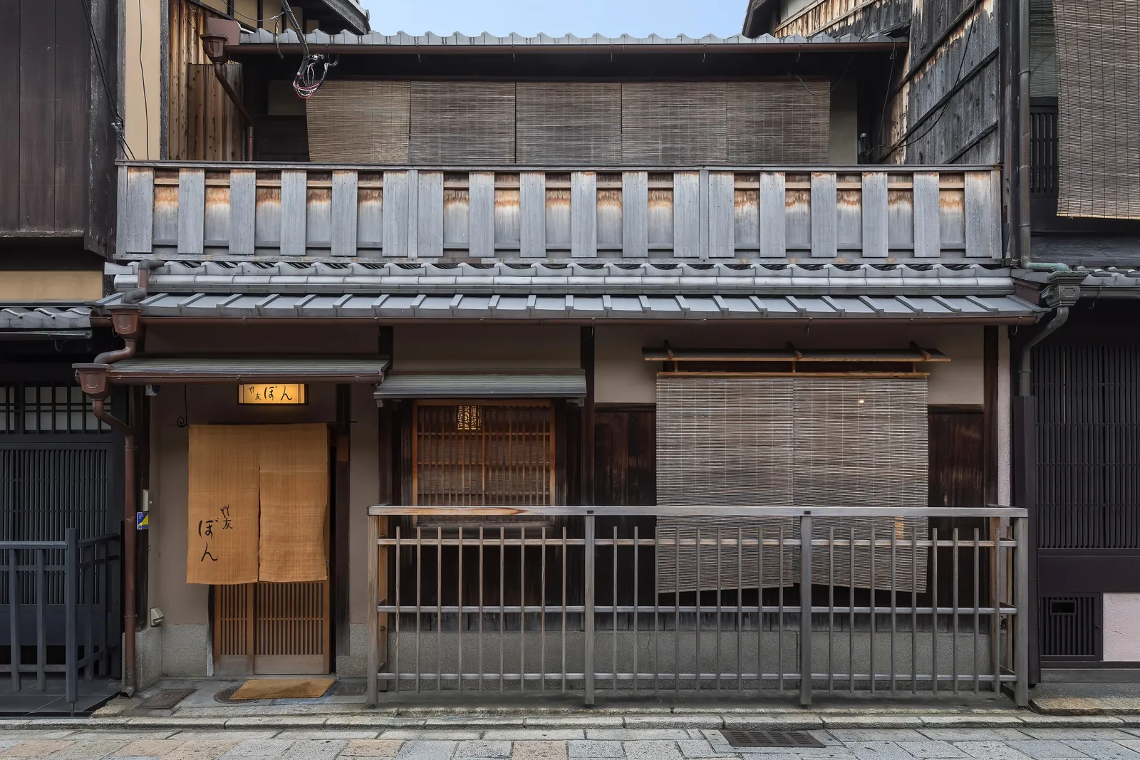 The wooden facade of a traditional townhouse on Shinbashi-dōri in Gion, with bamboo blinds, wooden balustrades and a yellow lamp